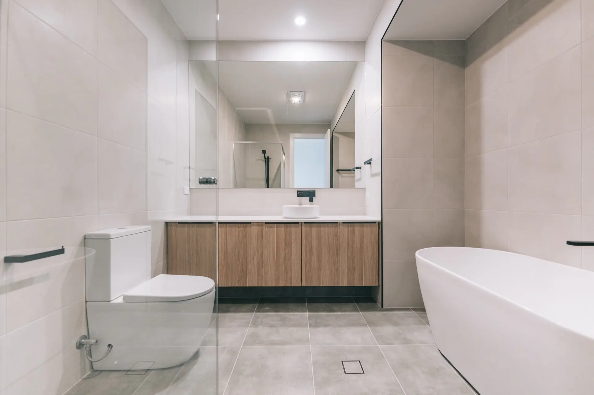 Bathroom with freestanding bath, timber vanity and black fixtures.