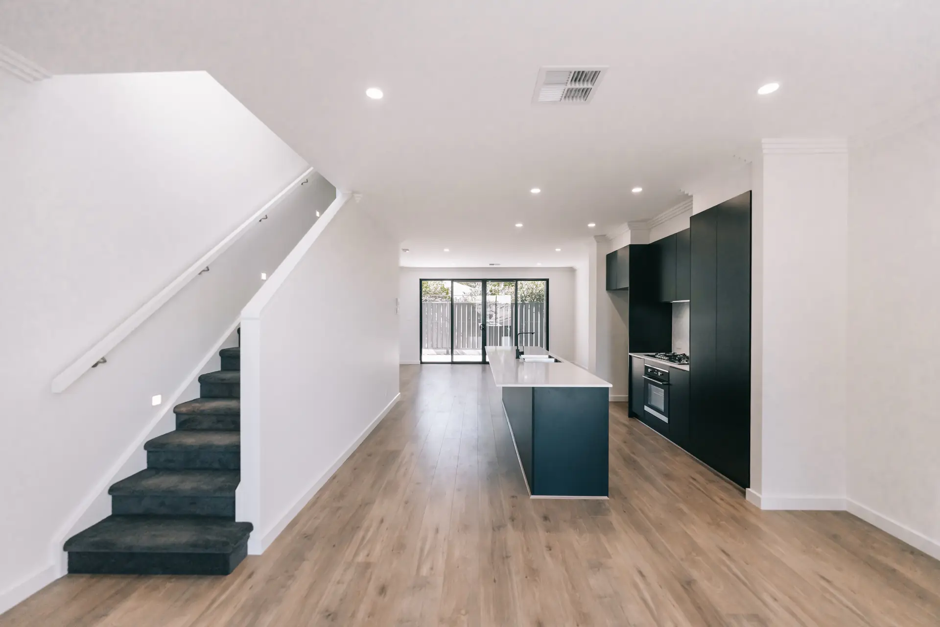 Open plan Colton Avenue living and kitchen with timber flooring and black cabinetry.