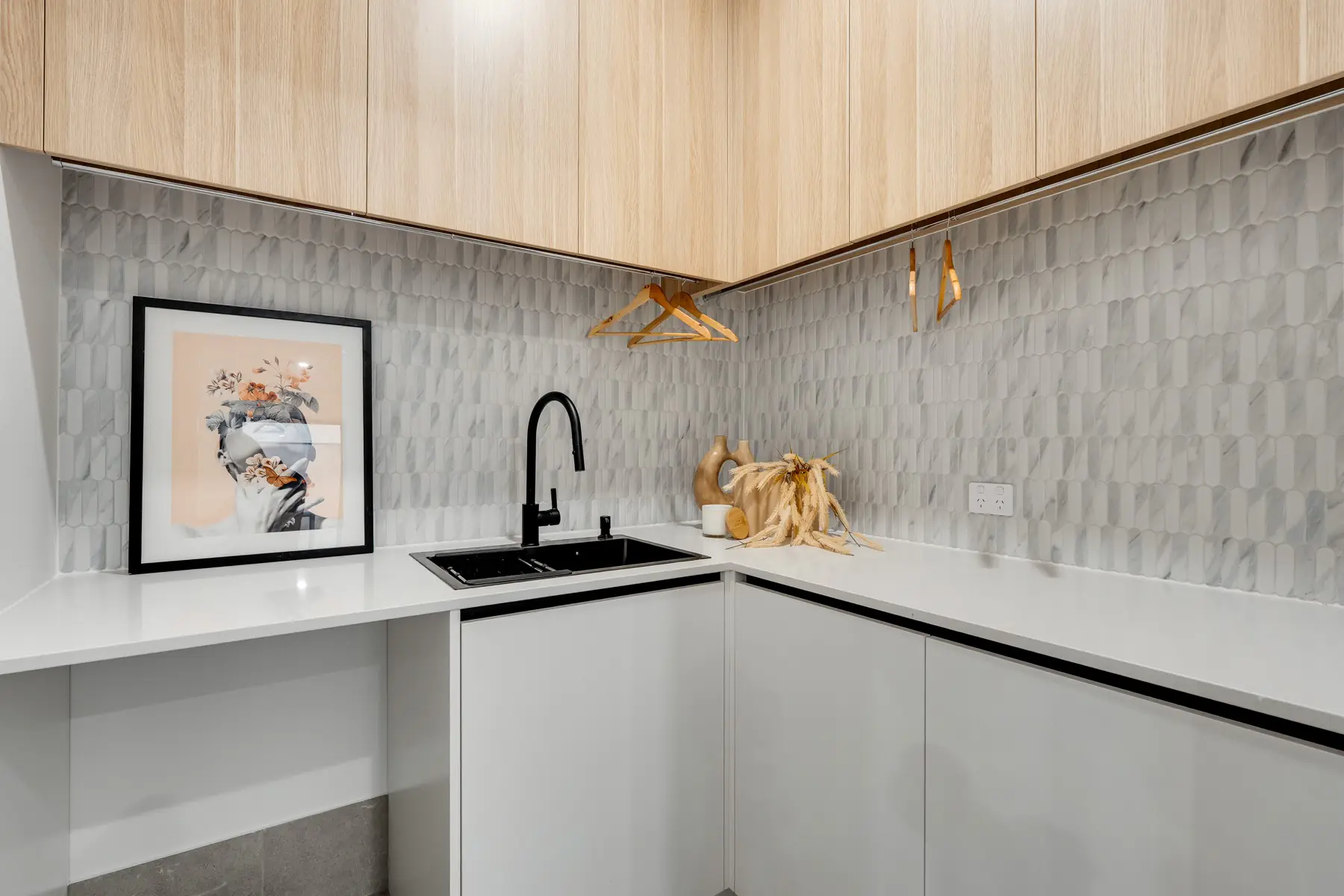 Kitchen detail with pale timber joinery, marble tile and black tapware.