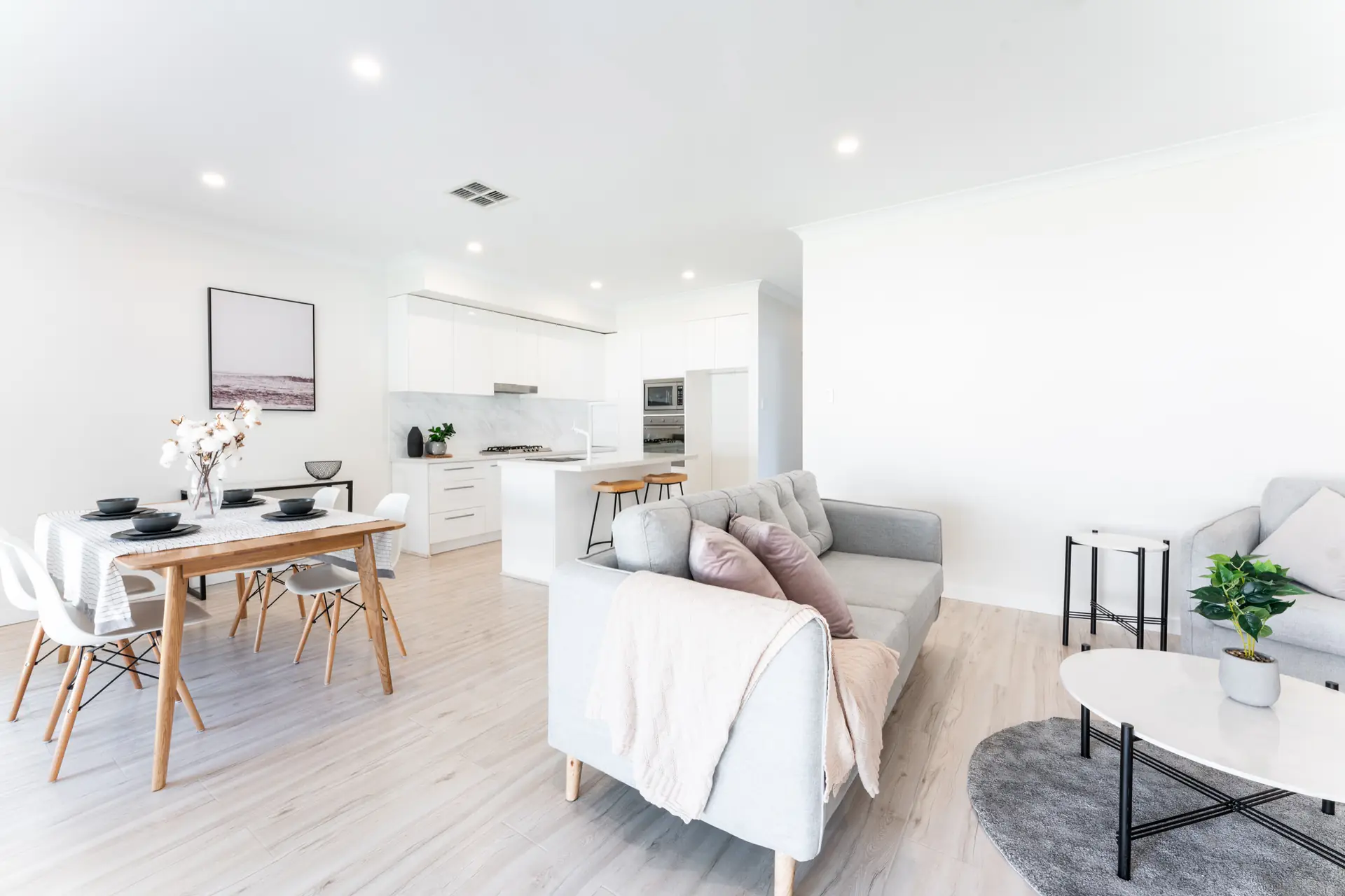 Living and dining room with pale timber flooring and white kitchen beyond.